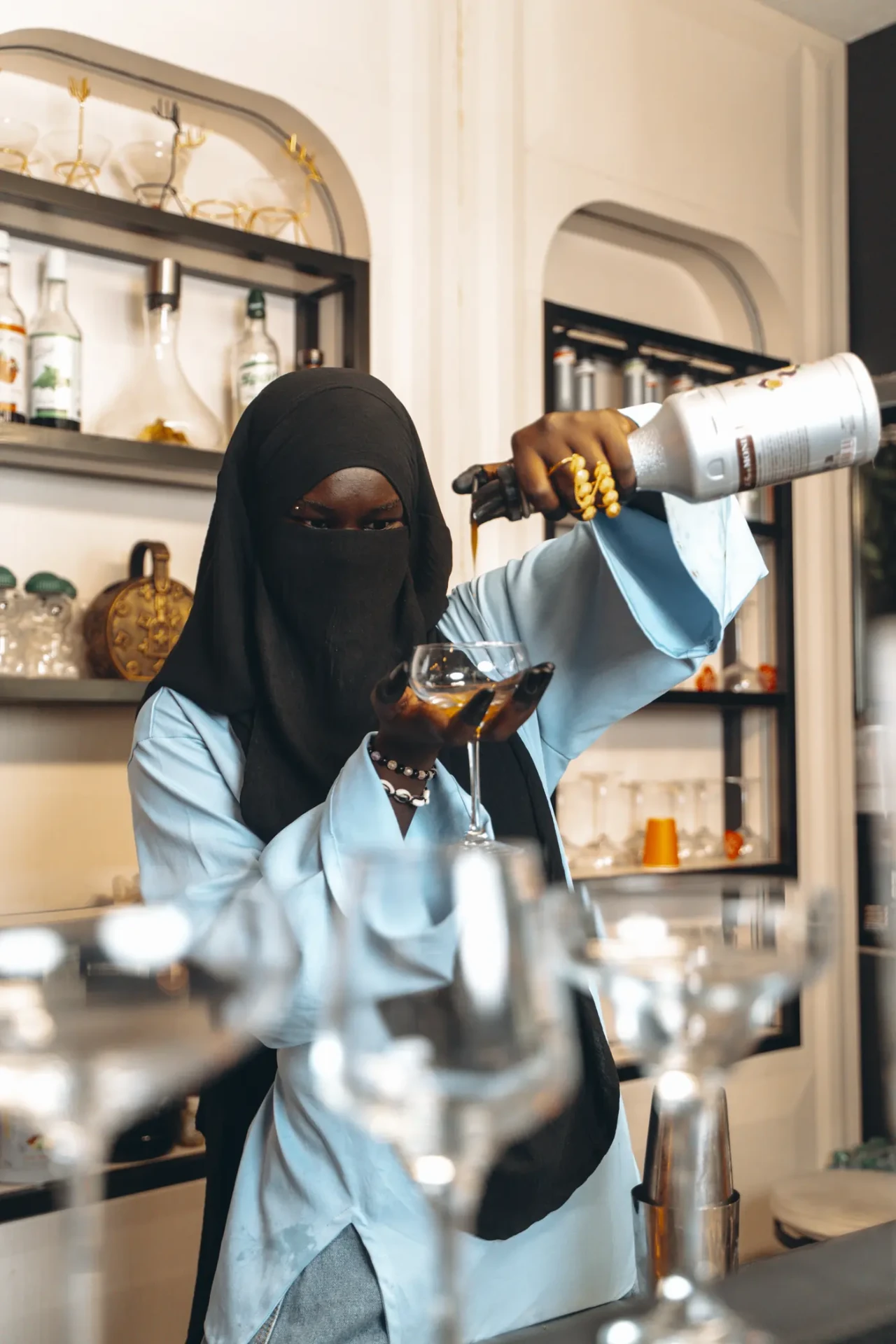 Penda Carlol verse un cocktail dans un verre derrière un bar clair