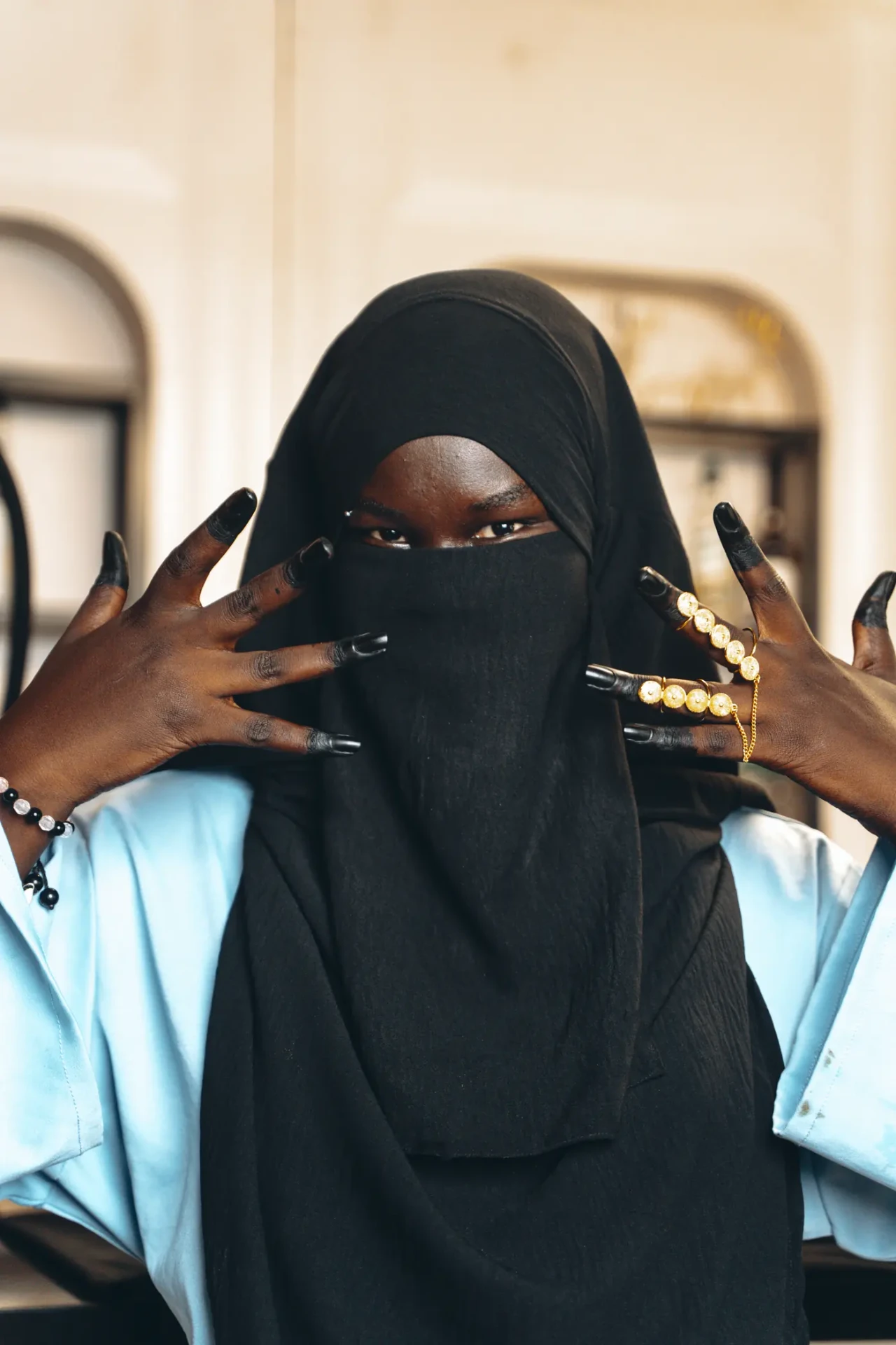 Portrait rapproché de Penda Carlol, mains levées près du visage, bagues dorées