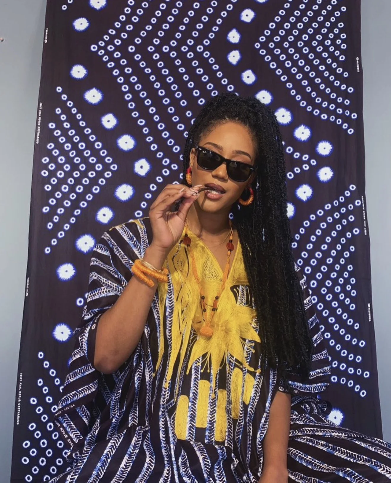 Amy Lucia Diop en boubou jaune et lunettes de soleil devant un tissu indigo à motifs blancs