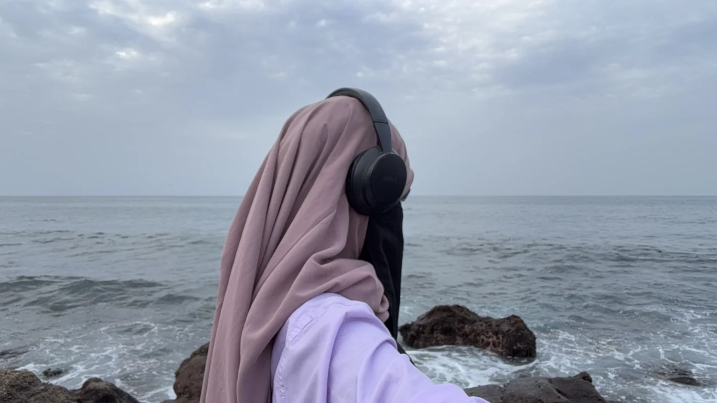 Penda Carlol de dos face à la mer, voile rose et casque audio, ciel nuageux