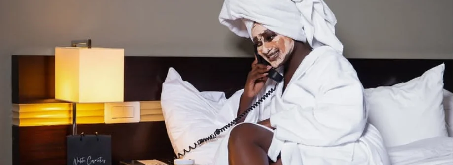 Chambre d'hôtel lumineuse, personne en peignoir au téléphone, bandeau d'ouverture Nabta Cosmetics