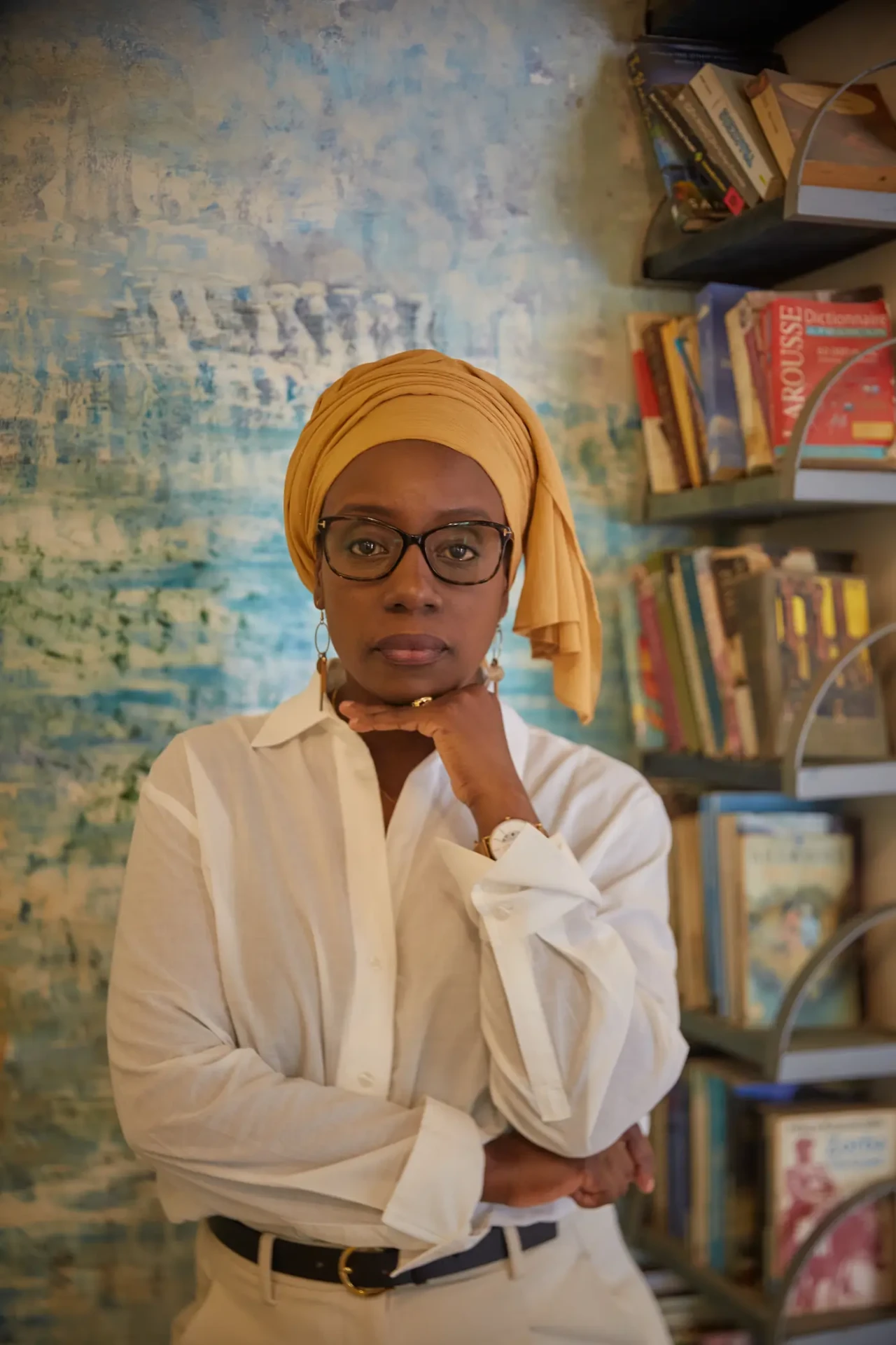 Portrait de la cliente en librairie, chemise blanche et foulard ocre, devant des étagères de livres