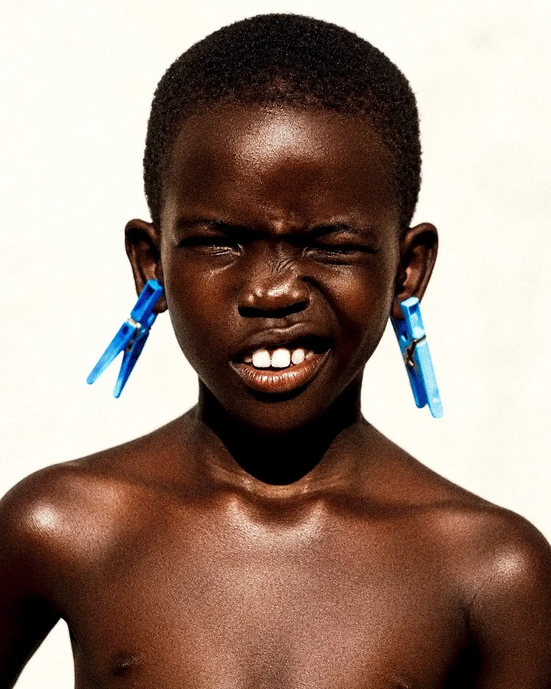 Portrait d'un enfant portant des pinces à linge bleues aux oreilles, fond crème