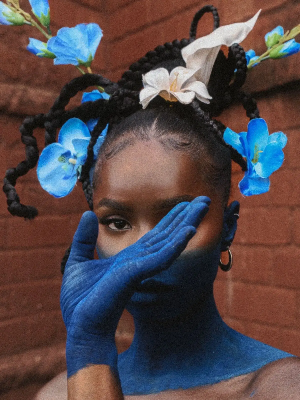 Portrait d'une femme aux tresses fleuries, mains gantées de bleu devant le visage